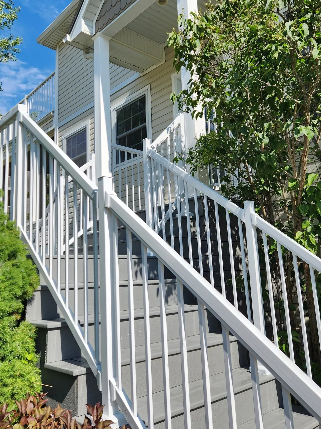New front deck stairs with white railings and grey steps beside a garden