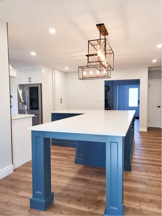 An open kitchen with a blue island under a cage pendant light, seen from the dining area