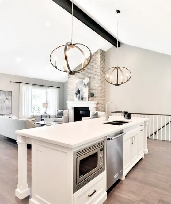 The finished white island with a sink and built-in stainless appliances, looking toward the brick fireplace beyond.