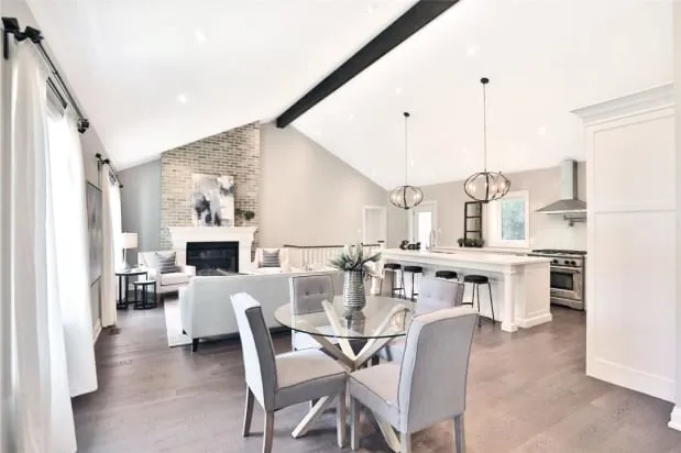 The open living and dining area with a brick fireplace, round glass table and the kitchen beyond.