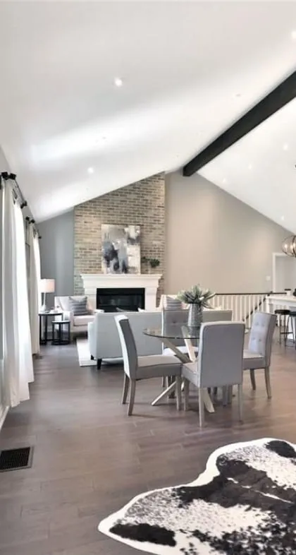 The living area's tall brick fireplace with a white mantel, seen past grey dining chairs and a glass table.