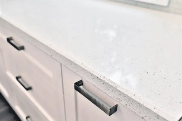 A close-up of a finished white flecked countertop above white drawers with dark bar pulls.