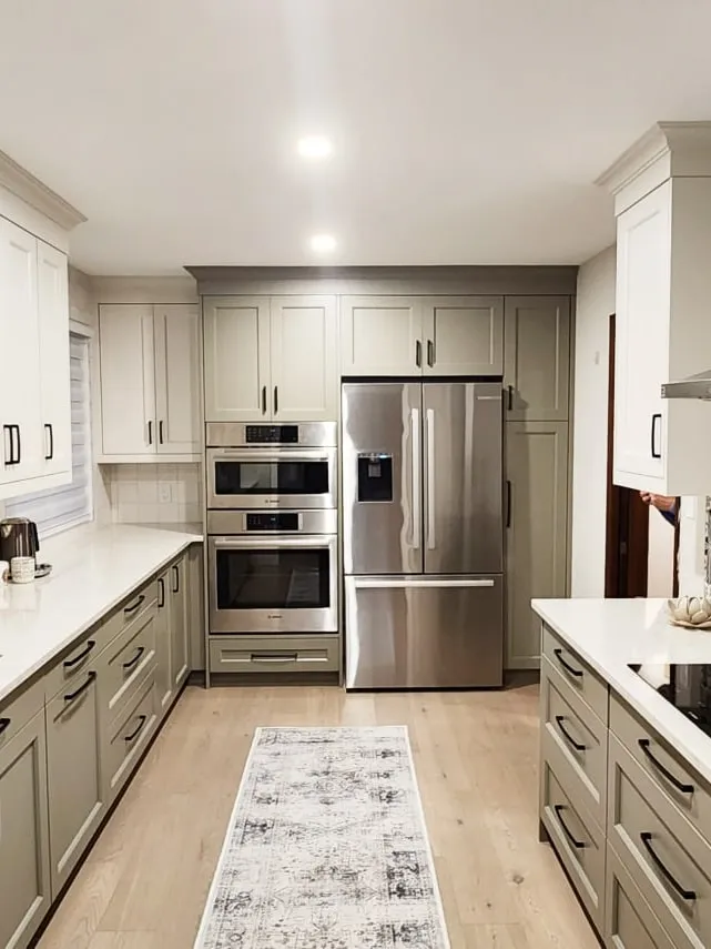 A long kitchen with sage lower cabinets, white uppers, a patterned backsplash and stainless appliances