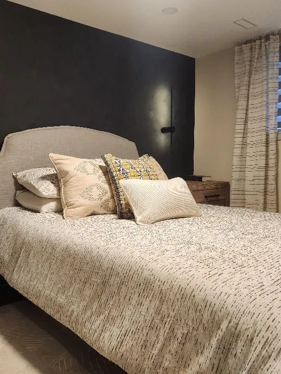 A finished basement bedroom with a dark feature wall, wall lights and a wide window