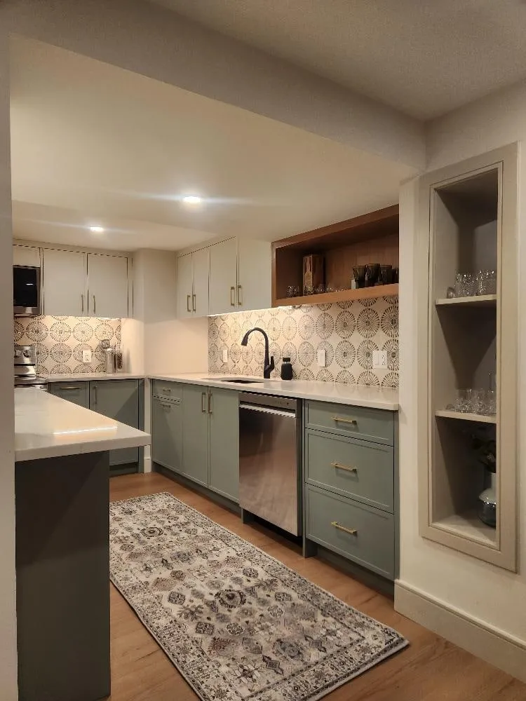 A kitchen with sage green cabinets, a patterned backsplash and a built-in display niche