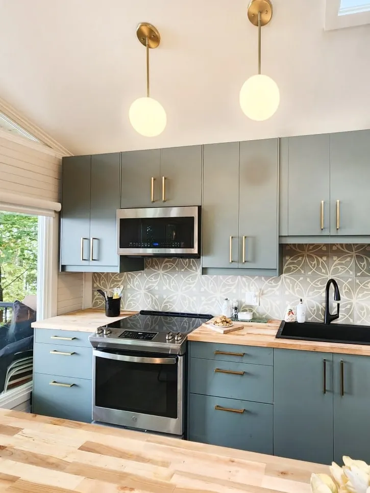 A cottage kitchen with sage cabinets, a butcher-block counter and two brass globe pendants